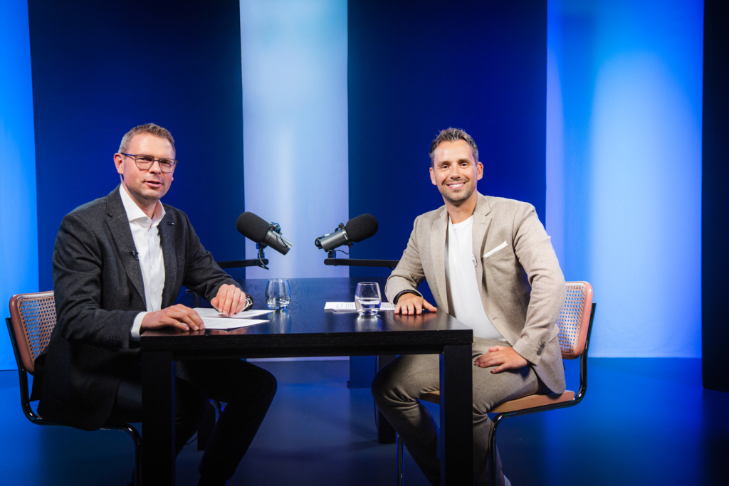 Das Bild zeigt Maximilian Kreitlmeier (Teamleiter Portfoliomanagement und Analyse, Fonds Finanz) und Daniel Arndt (Leiter Investment, Fonds Finanz) an einem Tisch sitzend mit Mikrofonen, wie sie den Videopodcast aufzeichnen.